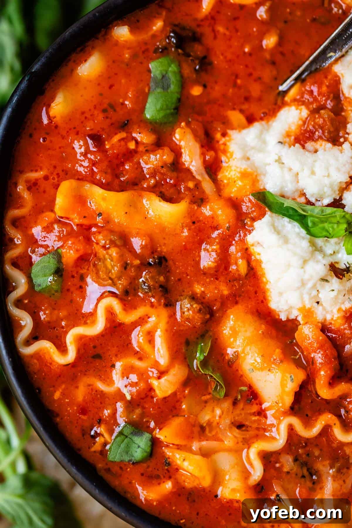The Definitive Lasagna Soup 17 A zoomed-in view highlighting the intricate details of lasagna noodles, creamy ricotta topping, and fresh basil garnish in a bowl of soup.