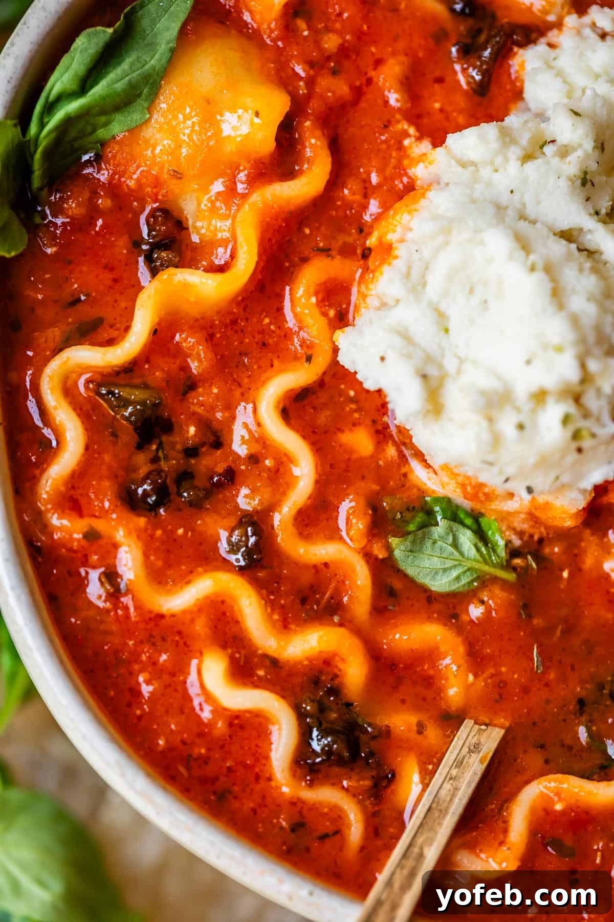 The Definitive Lasagna Soup 18 A ceramic bowl of lasagna soup with a soup spoon placed inside, inviting a comforting meal.