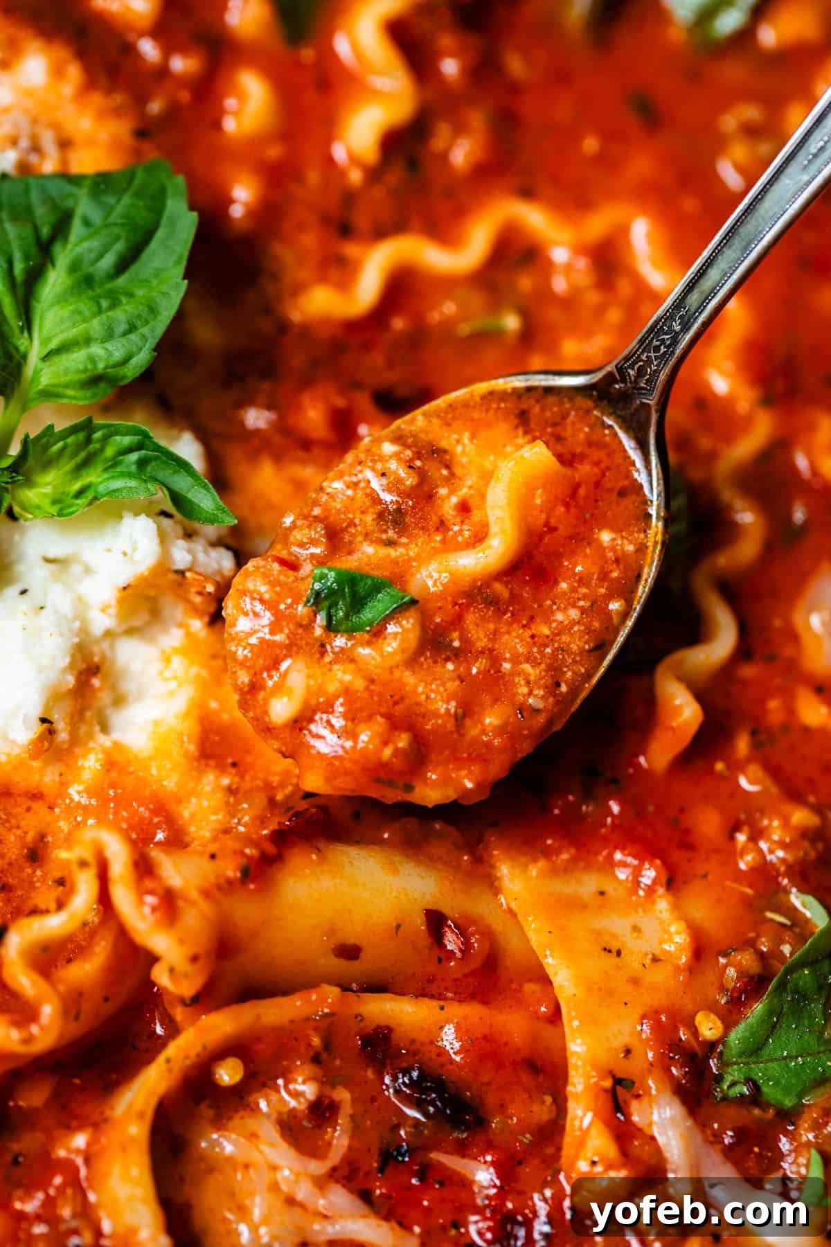 The Definitive Lasagna Soup 20 A metal spoon holds a scoop of rich marinara broth and a piece of noodle from the lasagna soup.