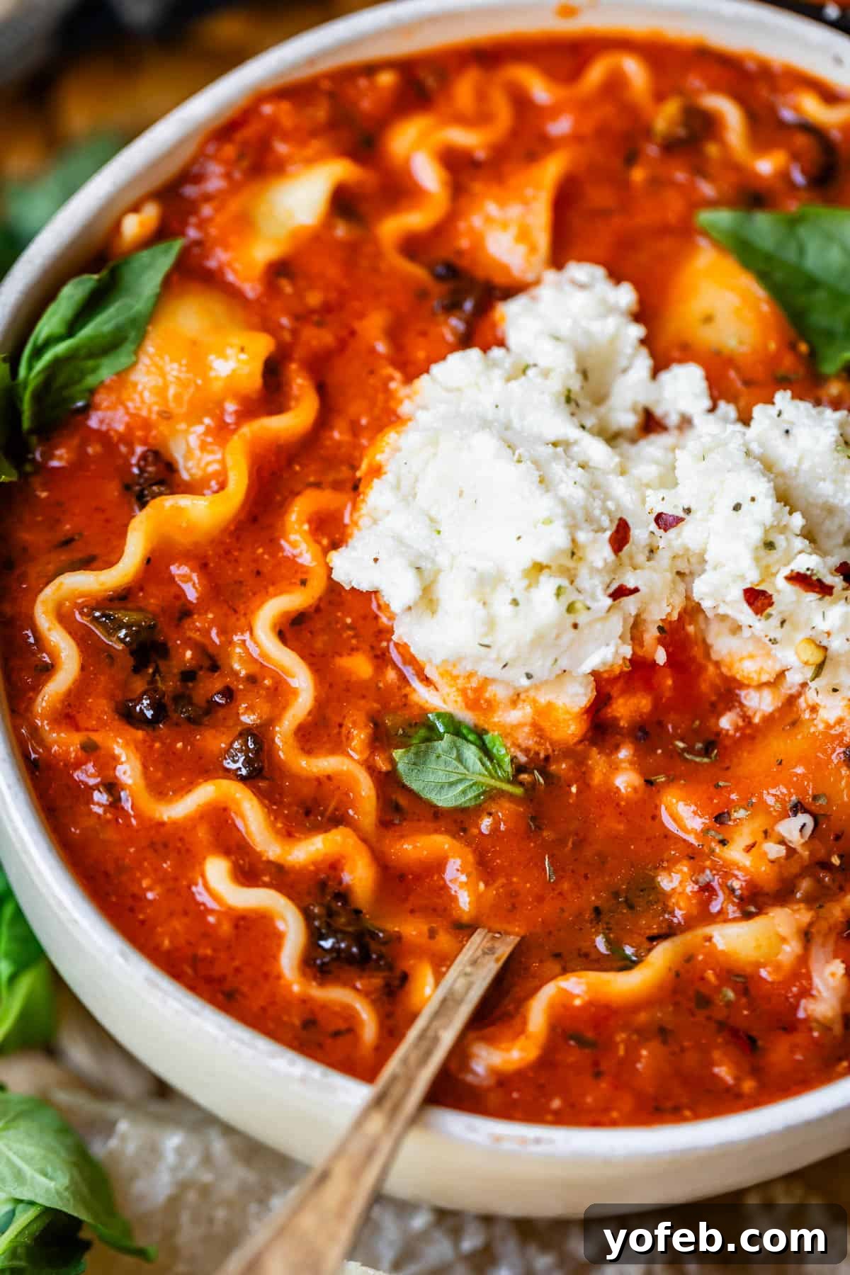 The Definitive Lasagna Soup 21 A ceramic bowl brimming with cozy lasagna soup, beautifully topped with creamy ricotta cheese.