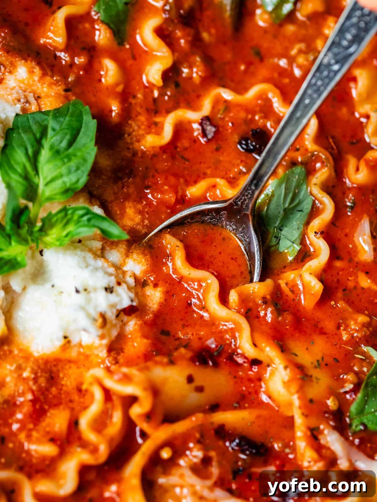 The Definitive Lasagna Soup 6 A metal spoon dipping into a bowl of lasagna soup, showcasing the noodles, broth, and cheesy topping.