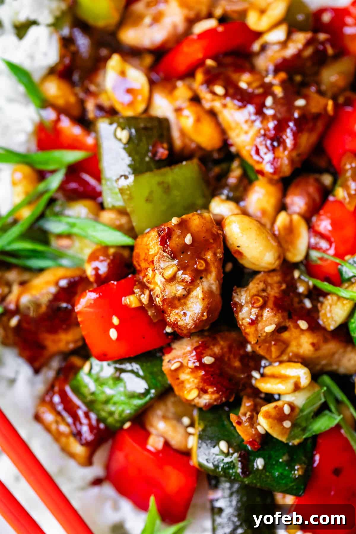 Szechuan Kung Pao Chicken 18 A close-up of a serving of Kung Pao chicken, featuring tender chicken, crunchy peanuts, and vibrant vegetables, with a pair of chopsticks resting nearby, inviting you to dig in.