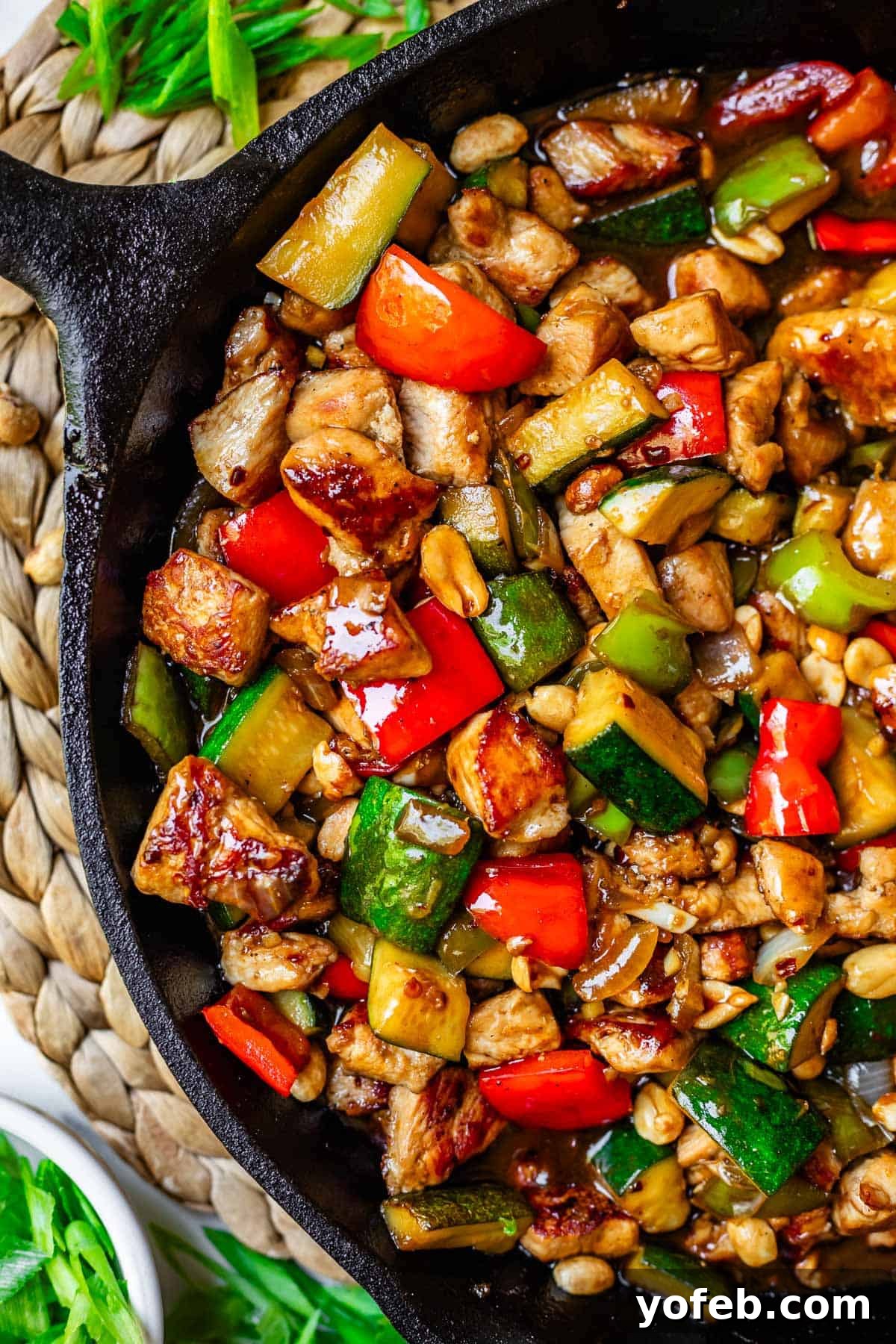 Szechuan Kung Pao Chicken 4 An inviting overhead shot of homemade Kung Pao chicken, showcasing succulent chicken pieces, vibrant zucchini and bell peppers, and crunchy peanuts glistening in a rich Asian sauce.