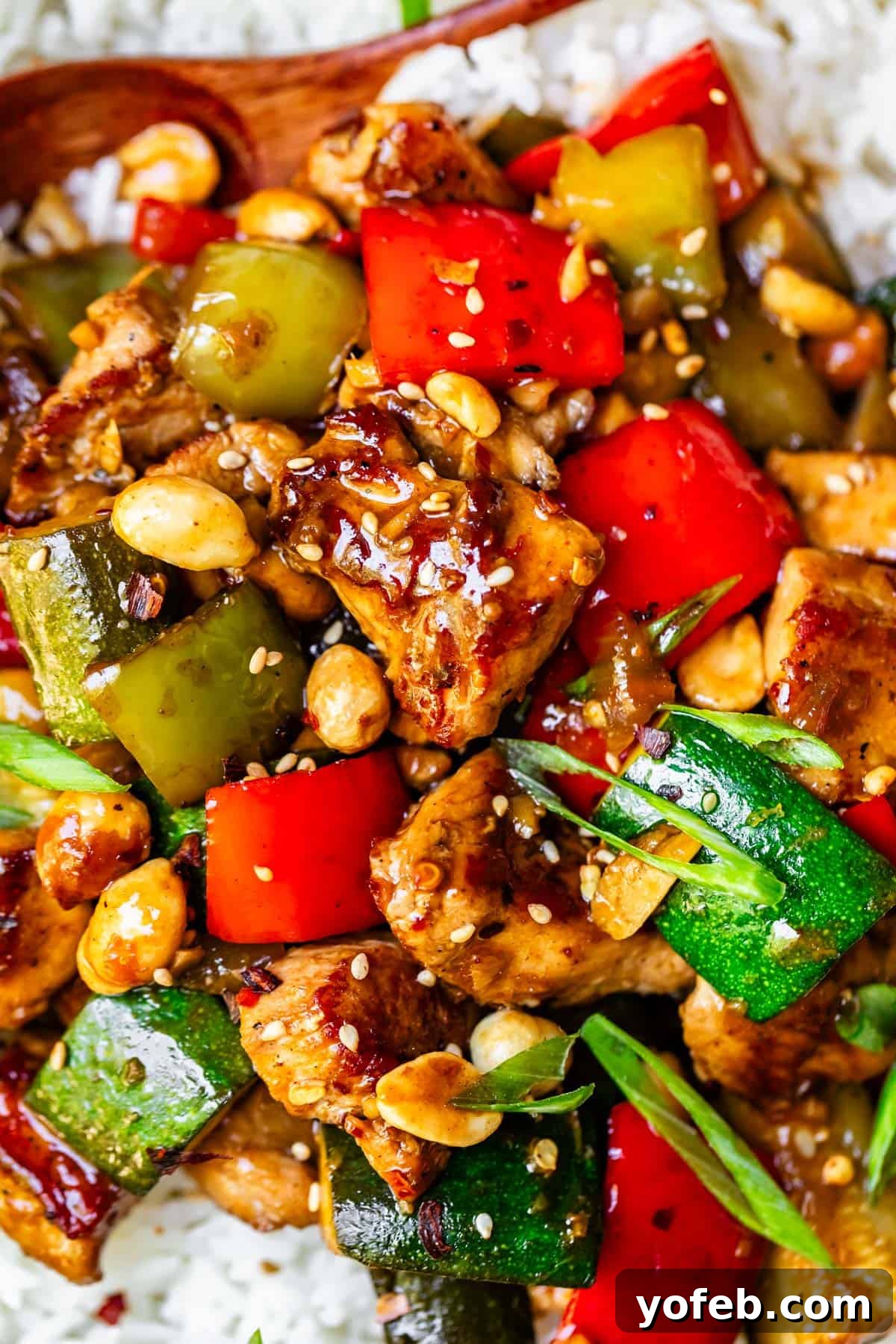 Szechuan Kung Pao Chicken 6 Saucy Kung Pao chicken with vibrant zucchini, red bell pepper, and peanuts, perfectly served over a bed of fluffy white rice.