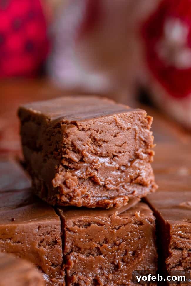 Mom's Effortless Fudge 2 A square of rich, creamy marshmallow fluff fudge resting atop a larger slab of freshly made fudge, inviting chocolate lovers to indulge.