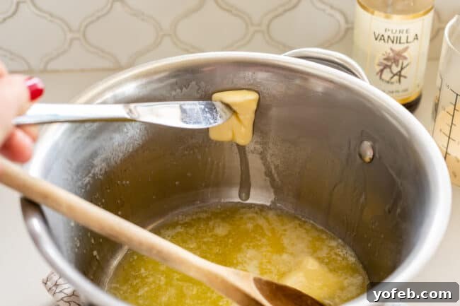 Mom's Effortless Fudge 14 A knife being used to spread melting butter along the edge of a pot, ensuring the sides are coated to prevent sugar crystallization.