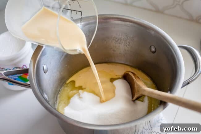 Mom's Effortless Fudge 16 Evaporated milk being poured from a measuring cup into a pot containing the butter and sugar mixture, initiating the next stage of fudge preparation.