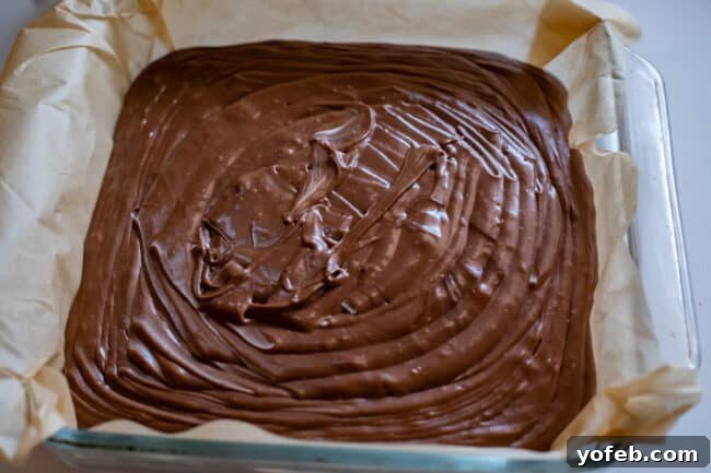 Mom's Effortless Fudge 25 Freshly poured fudge filling a glass pan lined with parchment paper, showcasing its beautifully rippled surface, ready to set.