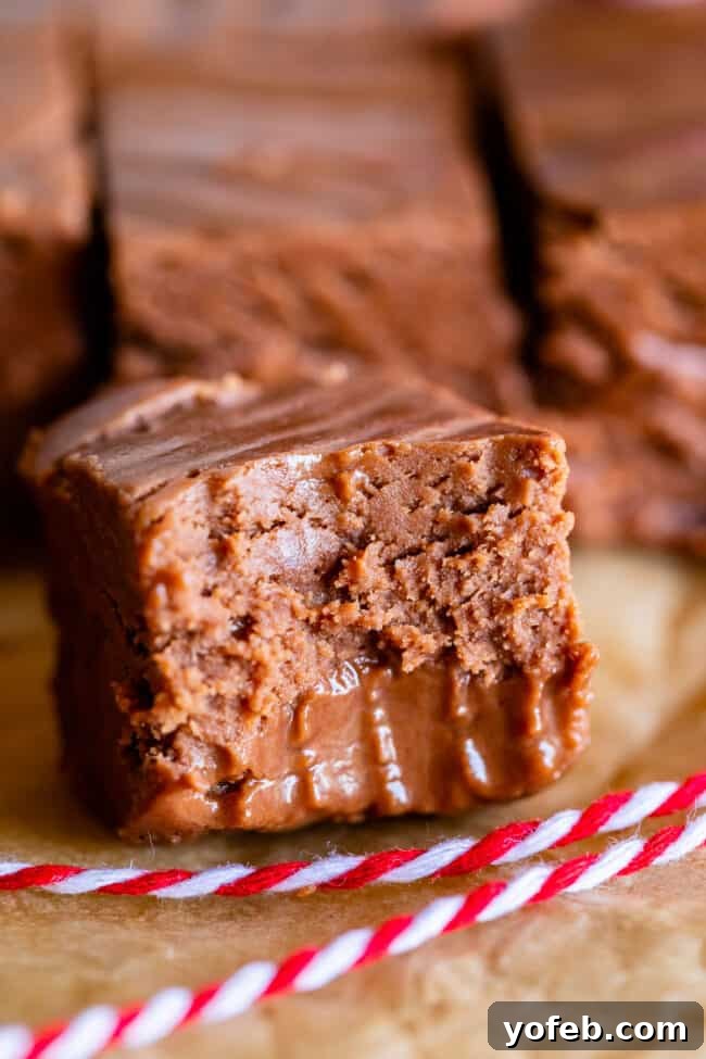 Mom's Effortless Fudge 4 A piece of creamy marshmallow fluff fudge with a bite taken out, resting on parchment paper alongside red and white baker's twine, evoking a festive, homemade feel.