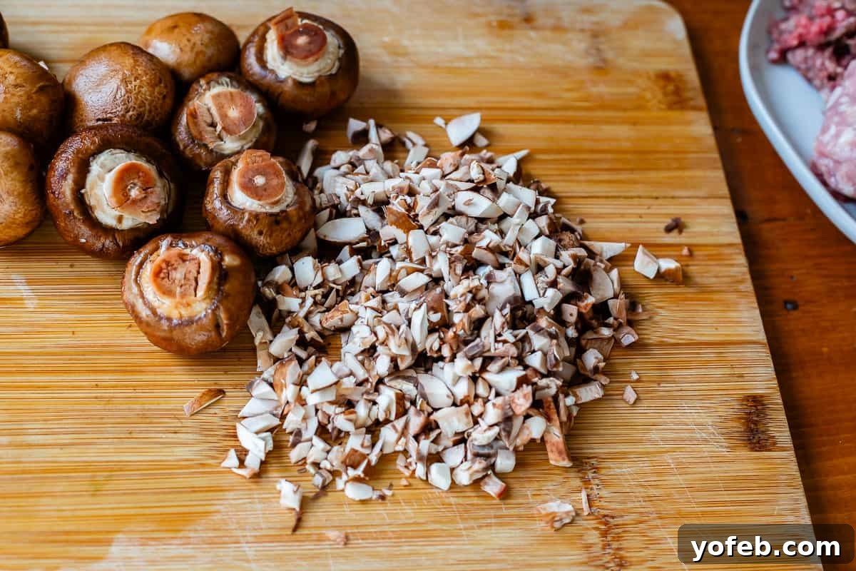 Grandma Prudy's Timeless Swedish Meatballs 17 Finely chopped mushrooms on a cutting board, with whole mushrooms blurred in the background, preparing to be added to the sauce.
