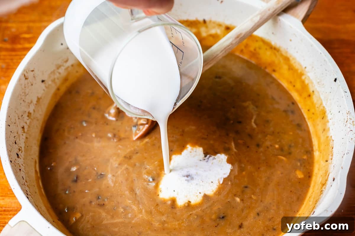 Grandma Prudy's Timeless Swedish Meatballs 20 A glass measuring cup elegantly pouring rich cream into the simmering gravy, transforming it into a luxurious, creamy sauce.