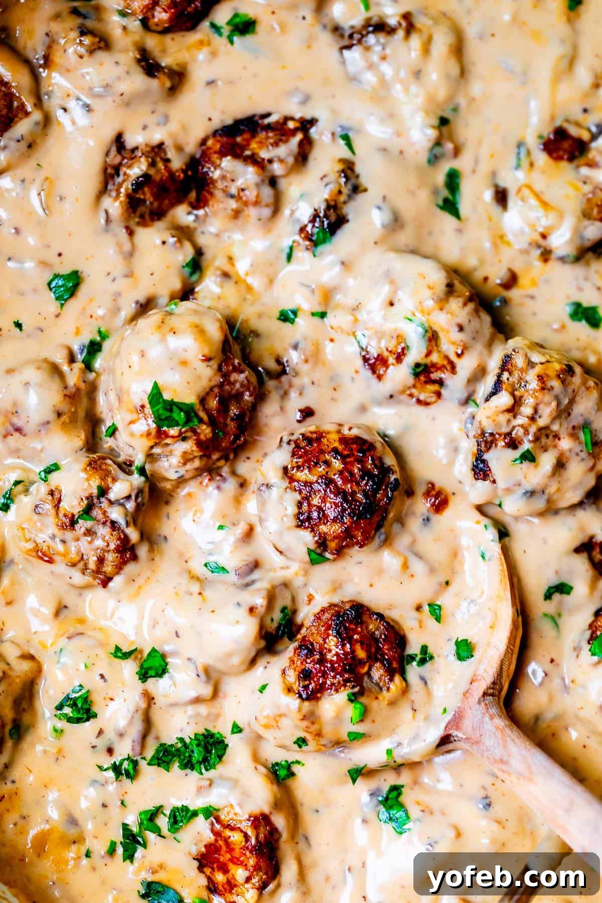 Grandma Prudy's Timeless Swedish Meatballs 24 A large wooden spoon gently stirring together creamy Swedish Meatballs and rich gravy in a skillet, ensuring every meatball is coated.