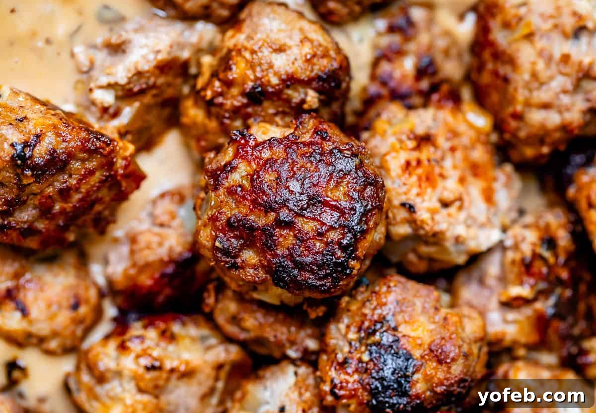Grandma Prudy's Timeless Swedish Meatballs 7 A close-up shot of a perfectly golden-brown fried Swedish meatball, with more cooked meatballs softly blurred in the background, hinting at their tender texture.
