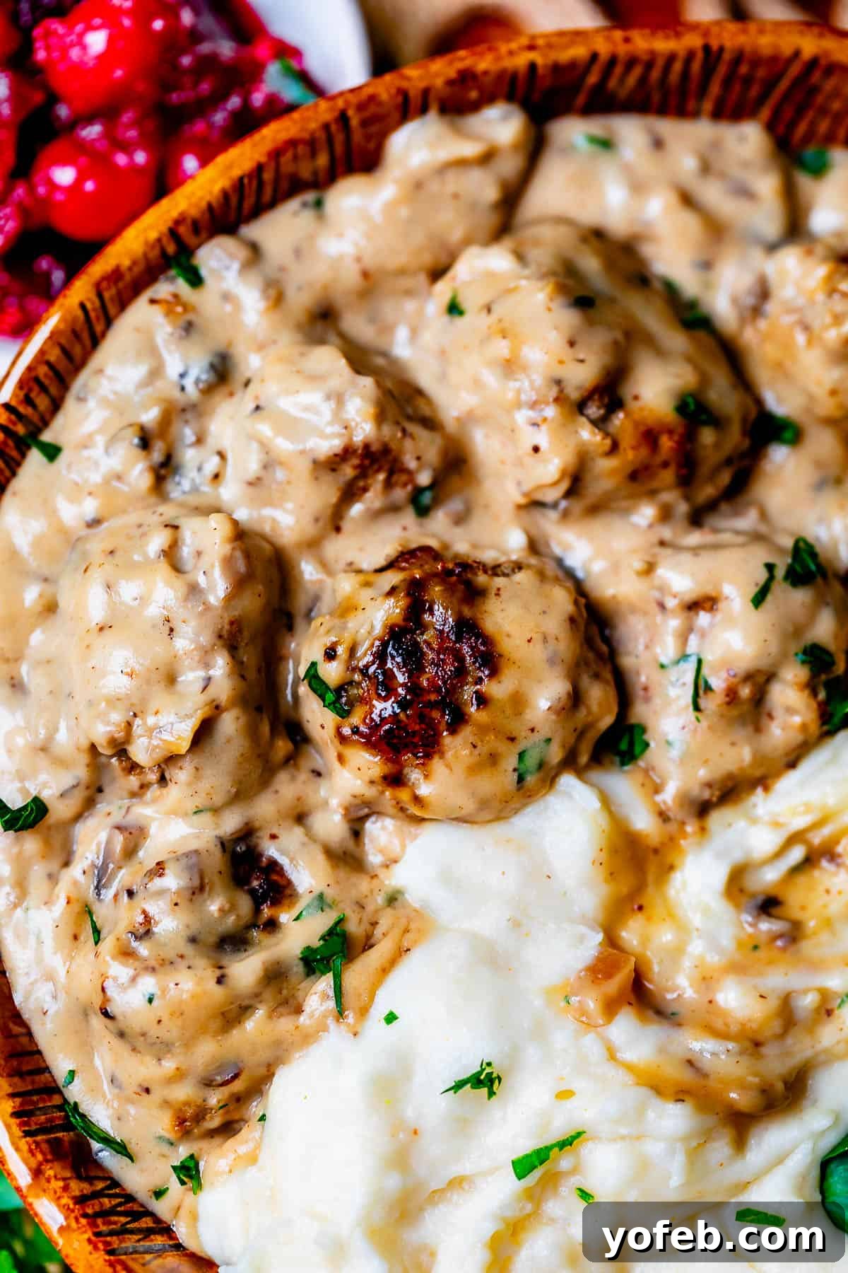 Grandma Prudy's Timeless Swedish Meatballs 10 A ceramic bowl showcasing Swedish Meatballs in a luscious creamy gravy poured over a bed of fluffy mashed potatoes.