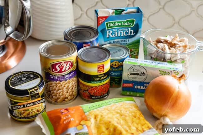 Effortless Creamy White Chicken Chili 8 Ingredients for white chicken chili recipe laid out on a kitchen counter, including canned beans, corn, onion, and spices.