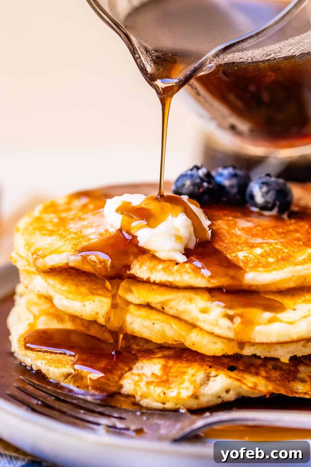 Effortless Homemade Maple Syrup 12 Homemade maple syrup being poured generously over a stack of fluffy pancakes, topped with a melting pat of butter and fresh blueberries, creating a tempting breakfast scene.