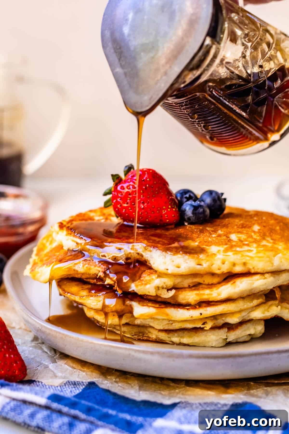 Effortless Homemade Maple Syrup 3 A stream of homemade syrup being generously poured over a stack of golden pancakes, garnished with an array of fresh berries, creating an inviting breakfast display.