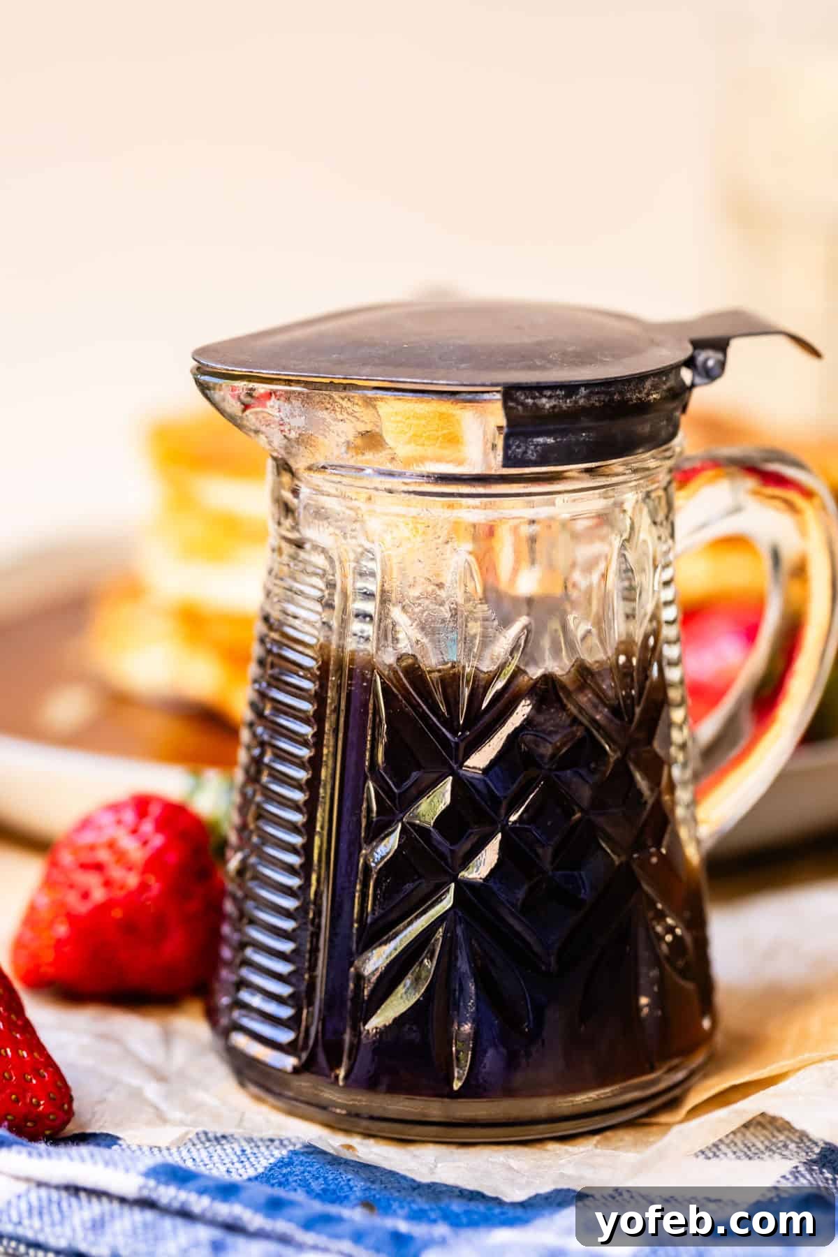 Effortless Homemade Maple Syrup 4 A glass pitcher filled with golden homemade syrup sits elegantly next to a vibrant assortment of fresh berries and fruit, ready to be enjoyed.