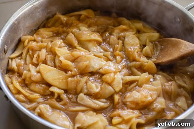 The Ultimate Dutch Apple Pie 19 Cooked apple pie filling is actively stirred in a pan with a wooden spoon, showcasing its rich, caramelized texture and even consistency.