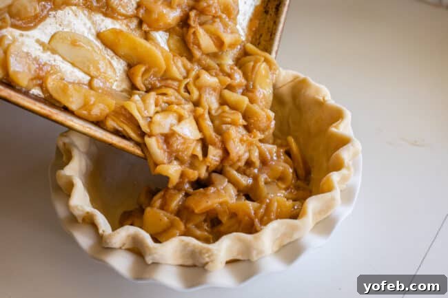 The Ultimate Dutch Apple Pie 22 Chilled apple pie filling is carefully scraped from a sheet pan into a frozen pie crust, ensuring all delicious gooeyness is transferred.
