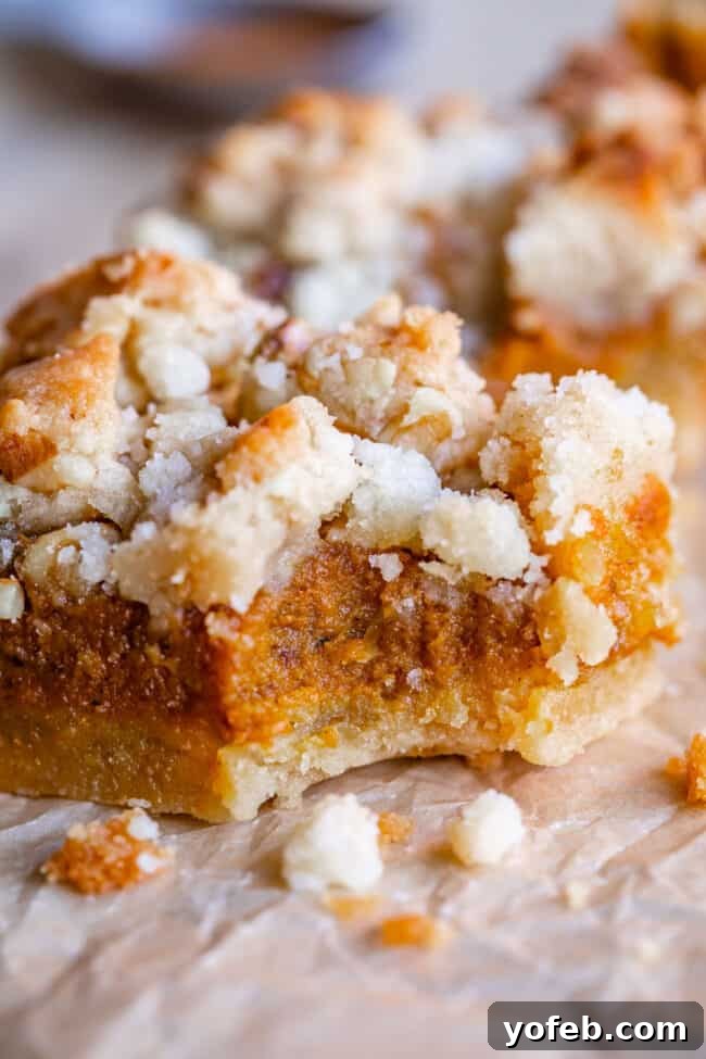 Buttery Pumpkin Spice Bars 3 Close-up of golden-brown pumpkin pie bars with a textured streusel topping and a visible shortbread crust layer, resting on parchment paper.