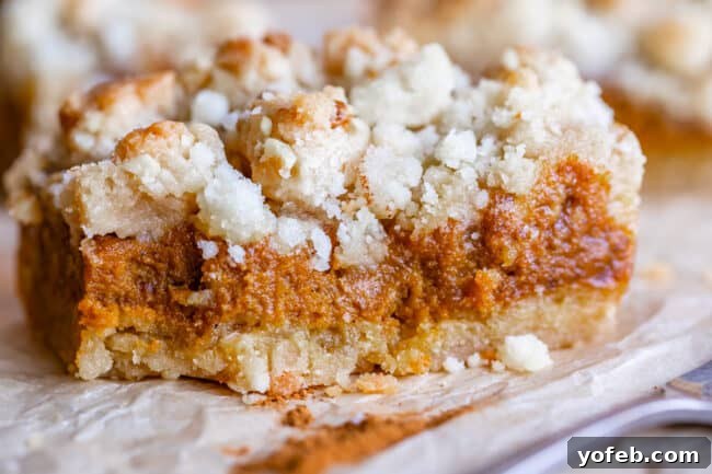 Buttery Pumpkin Spice Bars 6 A single square of pumpkin pie bar, perfectly portioned, resting on parchment paper with a fork beside it, showcasing its distinct layers and crumbly top.