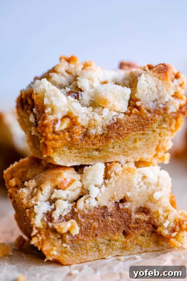 Buttery Pumpkin Spice Bars 9 A stack of golden pumpkin pie bars, showcasing the contrast between the thick shortbread crust and the smooth pumpkin filling, topped with streusel.