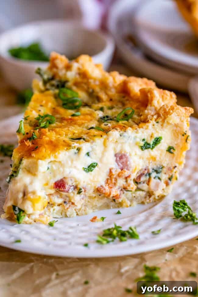 Effortless Bacon and Spinach Quiche 2 A large, tempting slice of homemade spinach and bacon quiche on a pristine white plate, garnished with fresh green onions.