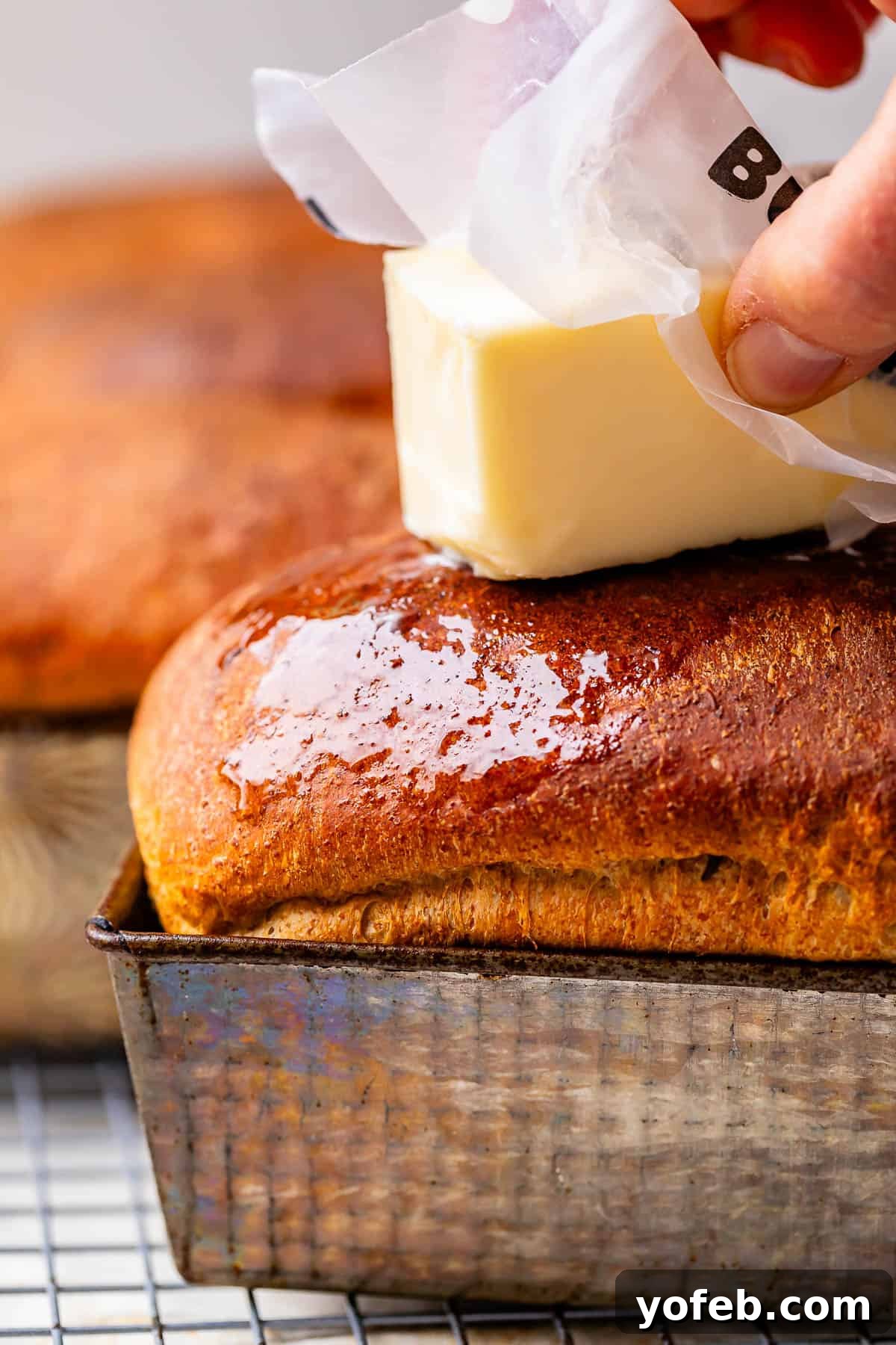 Grandma Prudy's Heirloom Rye Loaf 29 A stick of butter being rubbed over the tops of freshly baked rye loaves, creating a rich, melted glaze.
