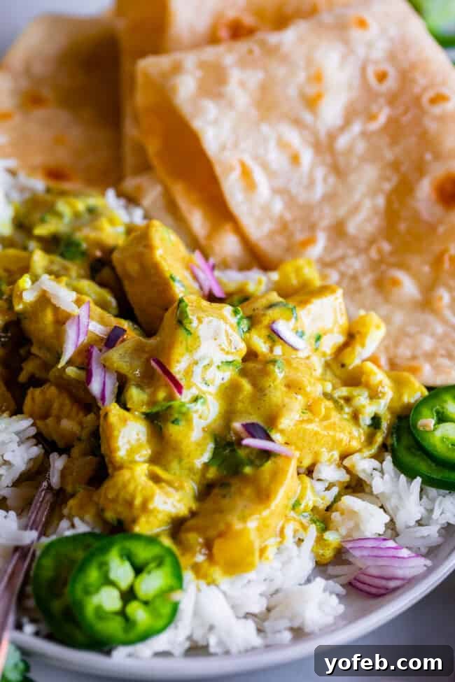 Flavorful Chicken Curry Made Easy 3 indian curry garnished with red onion and jalapeno on a plate with rice and roti.