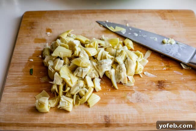 Ultimate Cheesy Spinach Artichoke Dip 13 Roughly chopped artichoke hearts arranged on a wooden cutting board, prepared for mixing into the dip.