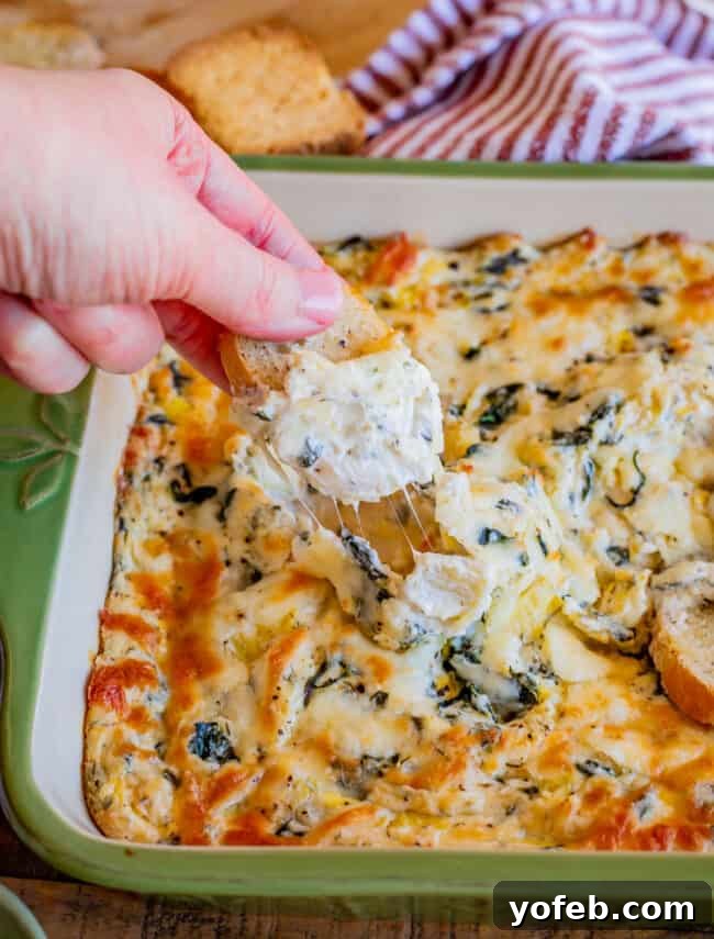Ultimate Cheesy Spinach Artichoke Dip 20 Hand dipping a piece of toasted bread into a bubbling hot pan of the best spinach artichoke dip.