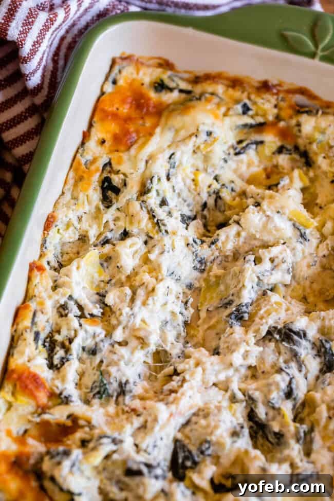 Ultimate Cheesy Spinach Artichoke Dip 21 A vibrant green casserole dish overflowing with hot, swirled spinach artichoke dip, ready to be served.