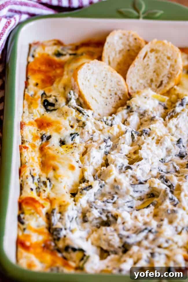 Ultimate Cheesy Spinach Artichoke Dip 4 Spinach and artichoke dip presented in a rustic green casserole dish, accompanied by three golden toasted bread slices.