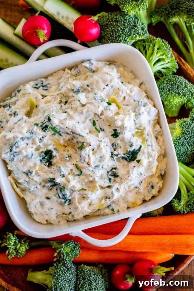 Ultimate Cheesy Spinach Artichoke Dip 7 Creamy spinach artichoke dip in a white serving bowl, elegantly surrounded by an assortment of fresh vegetables.