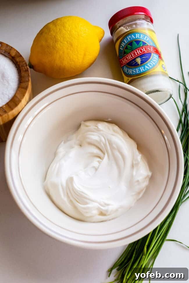 Fiery Homemade Horseradish Sauce 7 sour cream in a bowl with chives, lemon, salt, and jar of horseradish.
