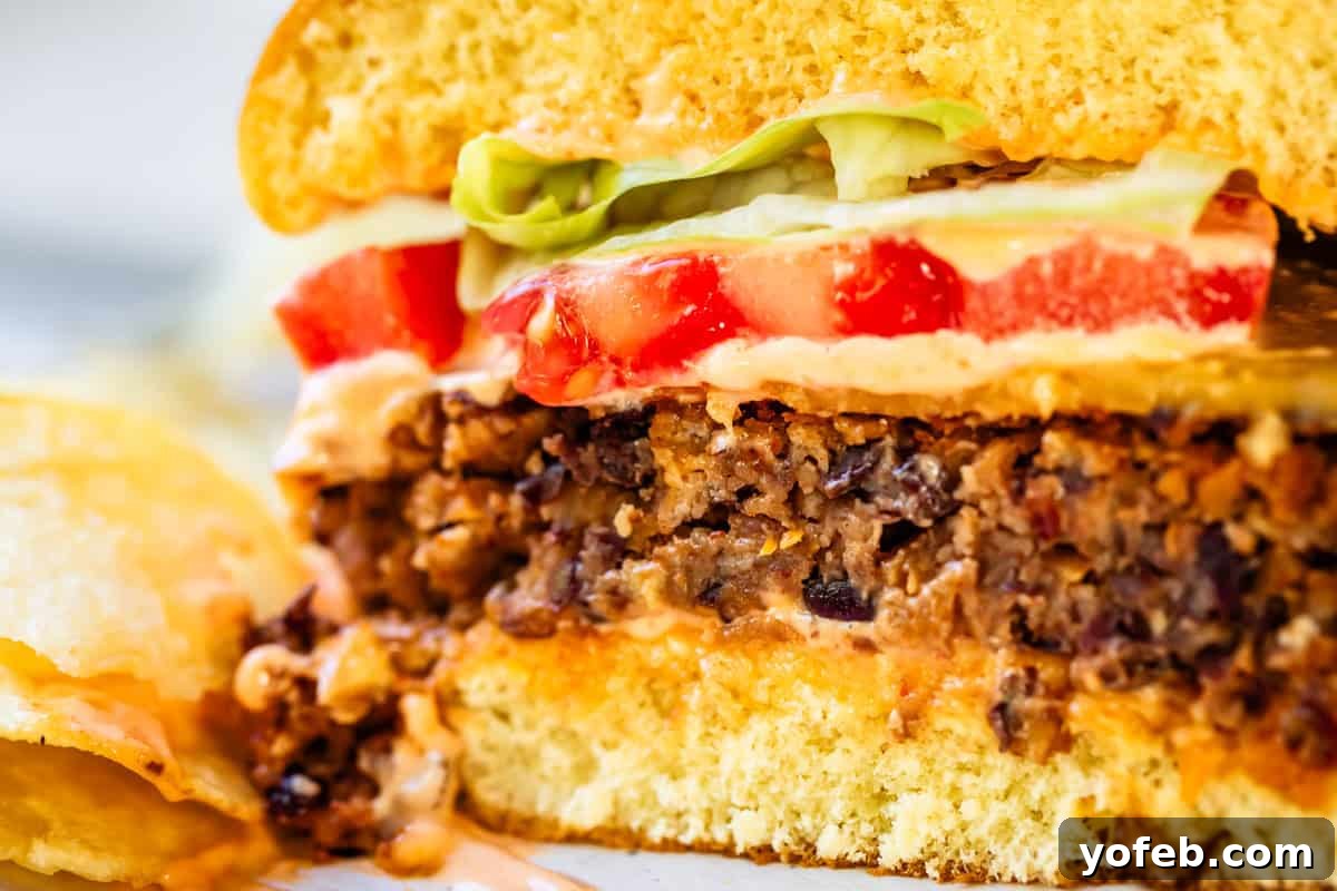 Savory Black Bean Burgers with Fiery Sriracha Aioli 11 A cross-section of a fully assembled black bean burger on a bun with melted cheese, fresh vegetables, and Sriracha mayo, served with a side of potato chips.