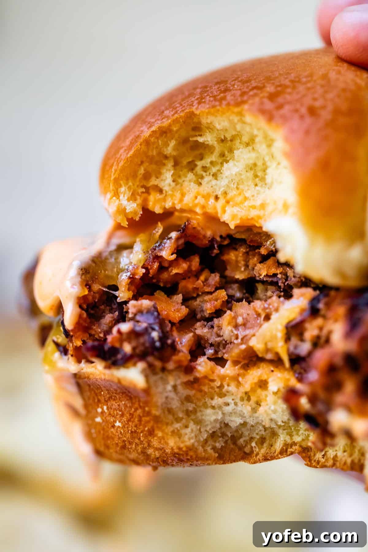 Savory Black Bean Burgers with Fiery Sriracha Aioli 13 A black bean burger on a bun, topped with cheese and sauce, with a bite taken out of it, showcasing its deliciousness.