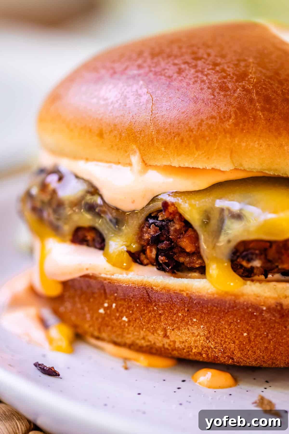 Savory Black Bean Burgers with Fiery Sriracha Aioli 4 A gourmet black bean burger on a toasted bun, featuring melted cheese and a generous drizzle of Sriracha mayo.