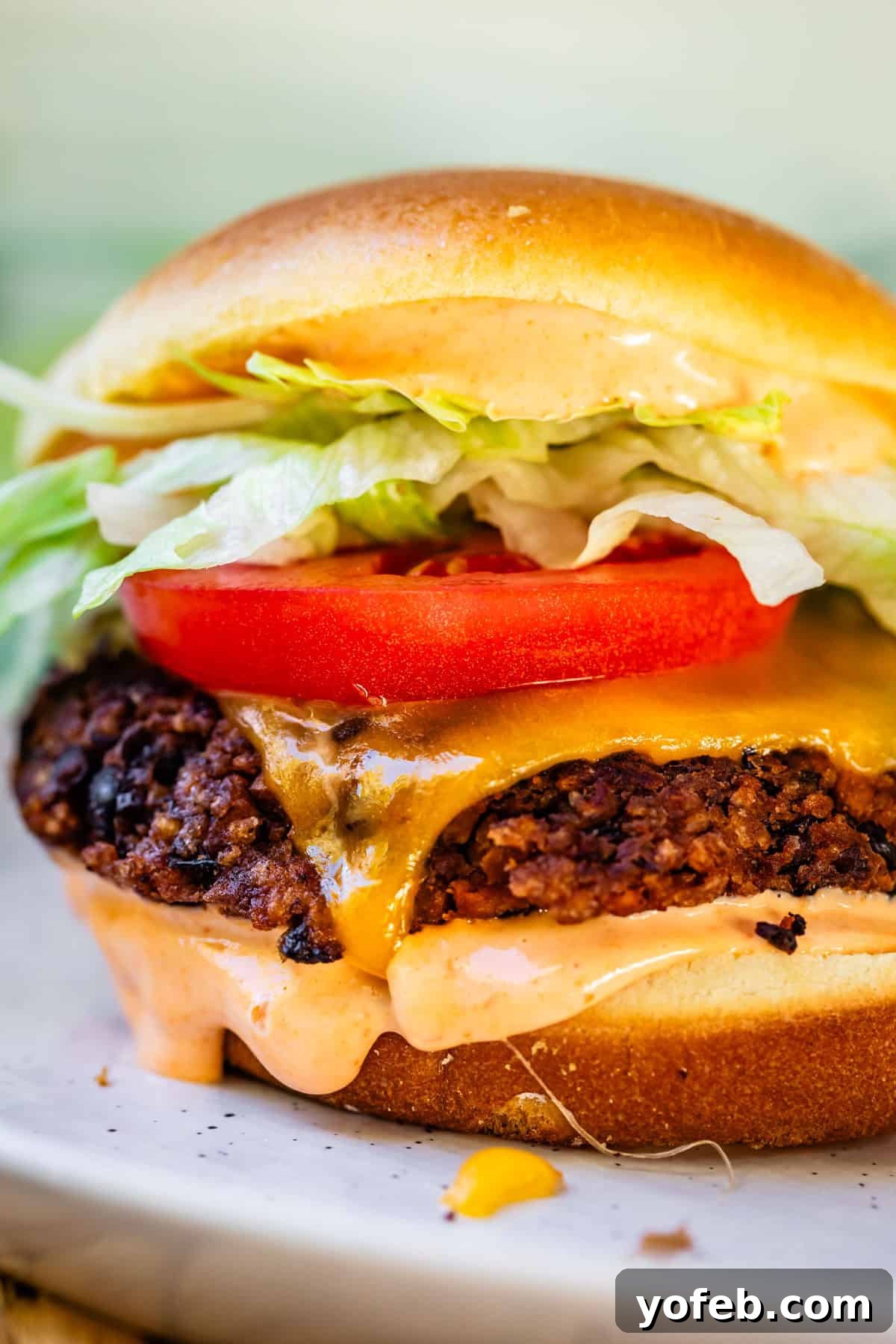 Savory Black Bean Burgers with Fiery Sriracha Aioli 5 A beautifully presented black bean burger, garnished with fresh vegetables, melted cheese, and a swirl of Sriracha mayo, accompanied by side dishes.