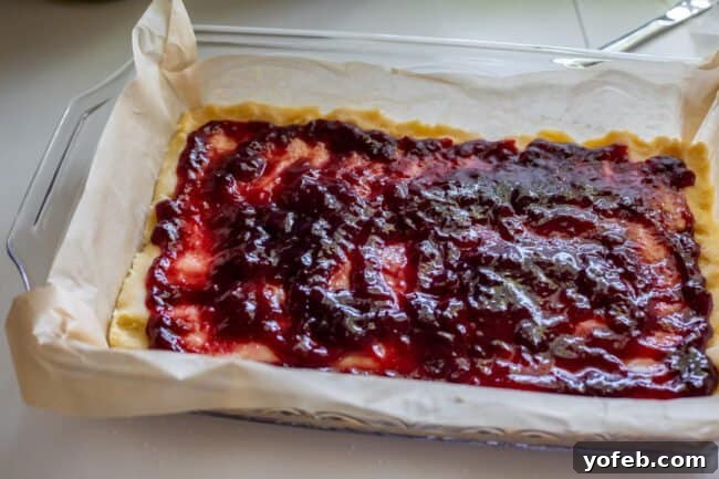 Almond Streusel Raspberry Crumb Bars 11 Partially baked shortbread crust pressed into a parchment-lined glass pan, topped with a layer of glistening raspberry jam.