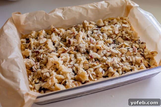 Almond Streusel Raspberry Crumb Bars 14 Unbaked raspberry crumb bars in a glass pan, showing the jam layer covered with almond streusel topping.