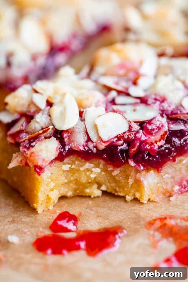 Almond Streusel Raspberry Crumb Bars 3 A single raspberry crumble bar on parchment paper, with a small bite taken out, showing the layers of crust, jam, and streusel.