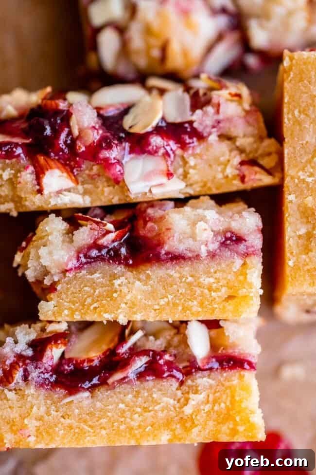 Almond Streusel Raspberry Crumb Bars 4 A stack of golden brown raspberry almond bars with visible jam layers, arranged neatly on parchment paper.
