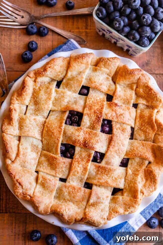 Grandma's Classic Blueberry Pie 3 An overhead shot of a freshly baked blueberry pie with a golden lattice crust, accompanied by a bowl of fresh blueberries, highlighting the pie's rustic charm.