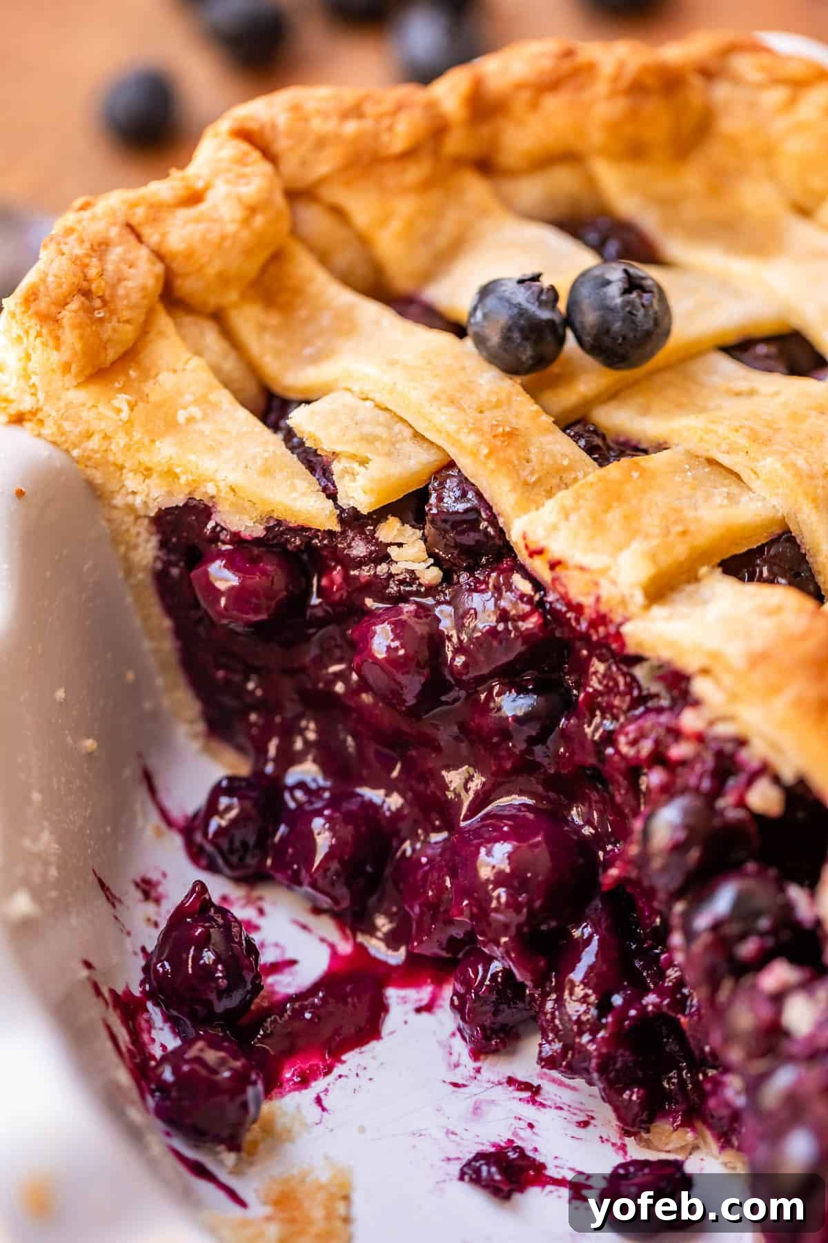 Grandma's Classic Blueberry Pie 4 A tantalizing image of a whole blueberry pie in a ceramic dish, with one slice already removed, revealing the juicy blueberry filling and sturdy crust. Fresh blueberries are scattered on top for garnish.