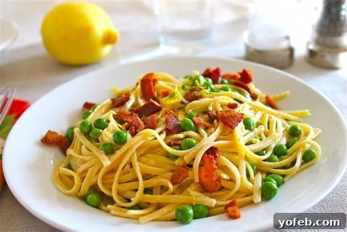Zesty Lemon Bacon Pea Pasta 3 Close-up of creamy lemon pasta with crispy bacon and vibrant green peas on a white plate, with a fresh lemon in the background.
