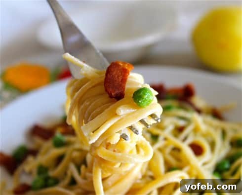 Zesty Lemon Bacon Pea Pasta 4 A forkful of creamy lemon bacon pasta, showcasing the perfect blend of ingredients, lifted from a full plate.