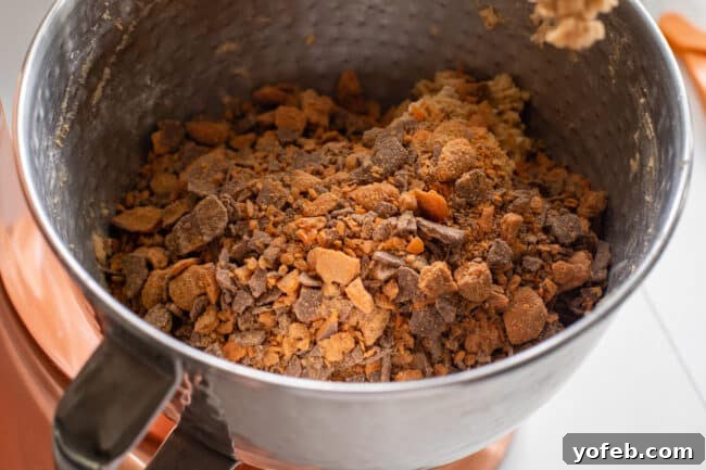 The Ultimate Peanut Butter Butterfinger Cookie 15 A large bowl of peanut butter cookie dough generously topped with crunchy Butterfinger Baking Bits, ready to be mixed in. This vibrant image showcases the abundance of candy in the cookie recipe.