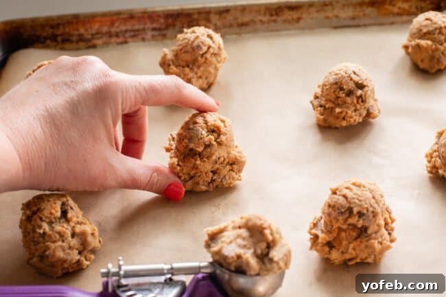 The Ultimate Peanut Butter Butterfinger Cookie 17 A hand gently places a perfectly portioned ball of Butterfinger cookie dough onto a parchment-lined baking sheet, alongside several other unbaked cookies. This image demonstrates the ideal size and placement for baking.